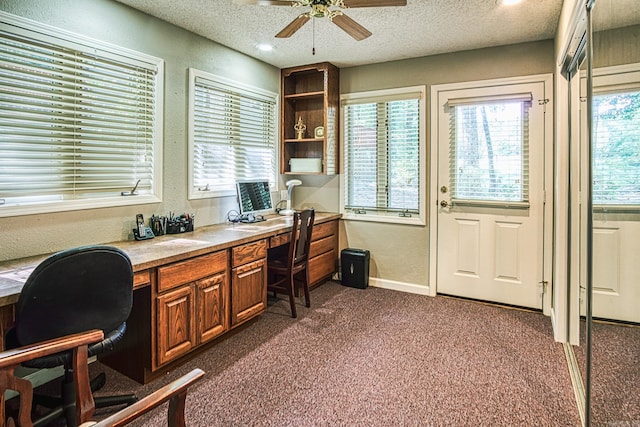 carpeted office featuring a wealth of natural light, built in desk, and a textured ceiling