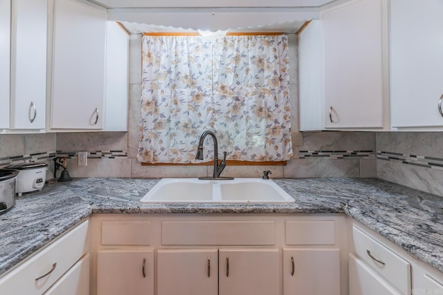 kitchen featuring light stone countertops, backsplash, sink, and white cabinetry