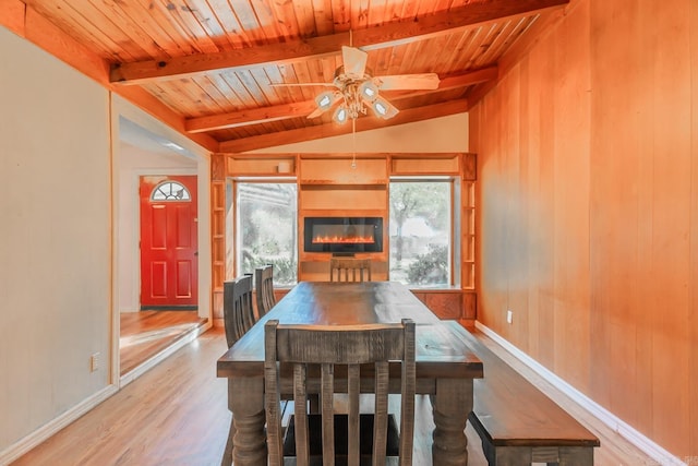 dining room with ceiling fan, vaulted ceiling with beams, wood ceiling, wooden walls, and light hardwood / wood-style flooring