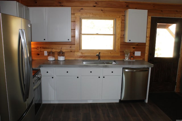 kitchen featuring sink, wood walls, white cabinetry, stainless steel appliances, and dark hardwood / wood-style flooring