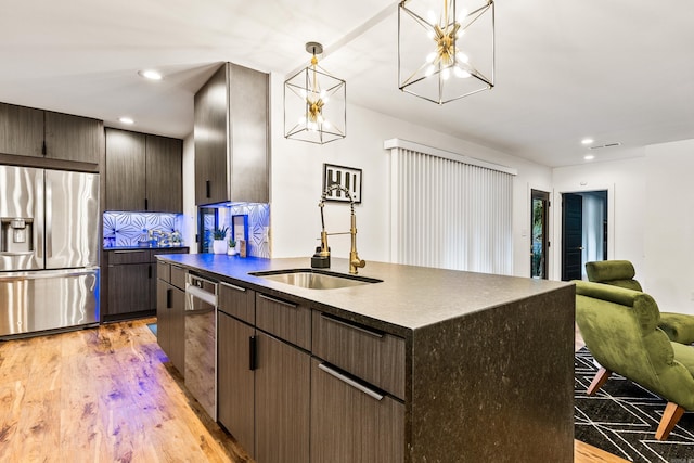 kitchen with pendant lighting, sink, light hardwood / wood-style flooring, stainless steel appliances, and a center island with sink