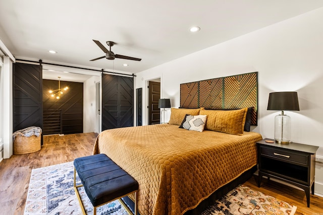 bedroom with a barn door, wood-type flooring, and ceiling fan