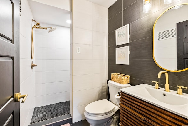 bathroom with vanity, a shower, tile walls, and toilet