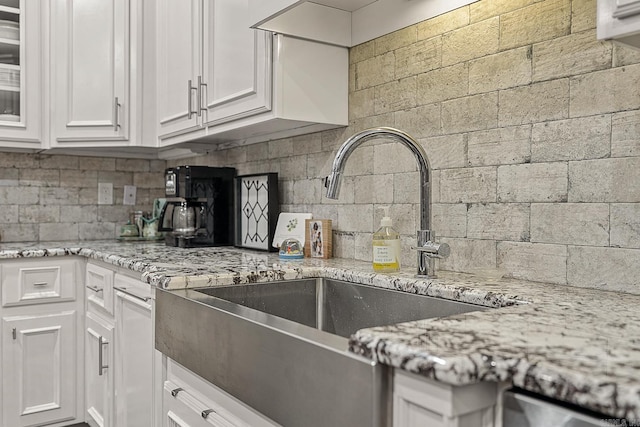 kitchen featuring light stone countertops, backsplash, sink, and white cabinetry