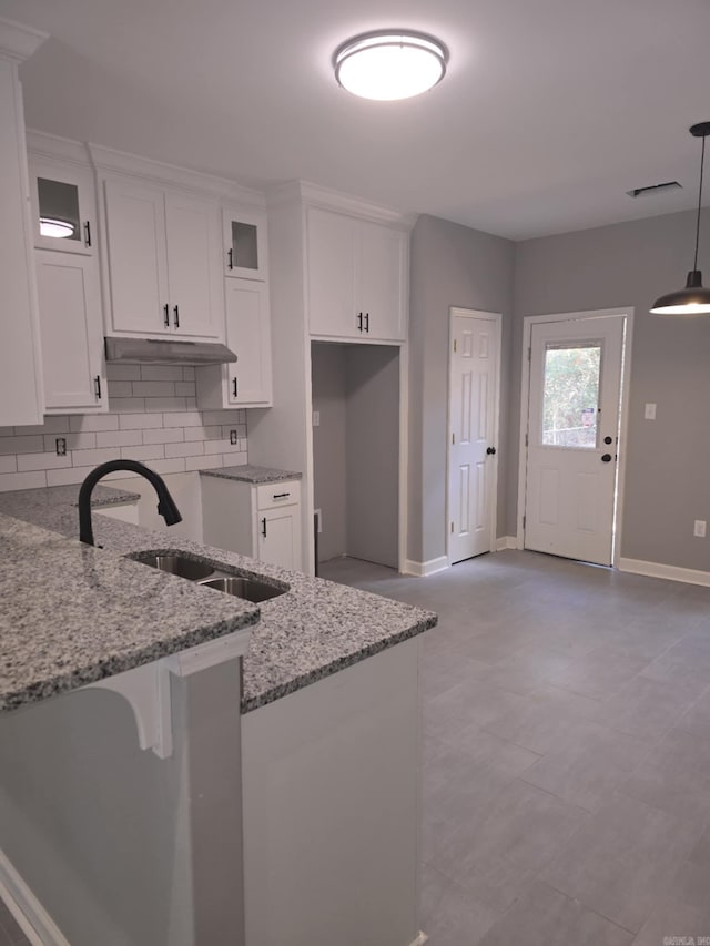 kitchen featuring tasteful backsplash, light stone counters, sink, pendant lighting, and white cabinets