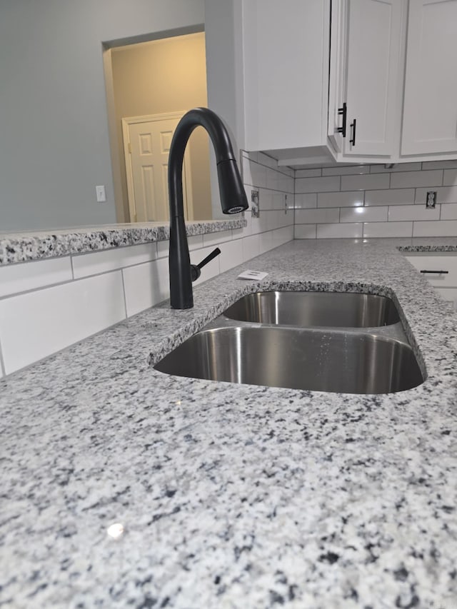 kitchen featuring decorative backsplash, light stone counters, sink, and white cabinets