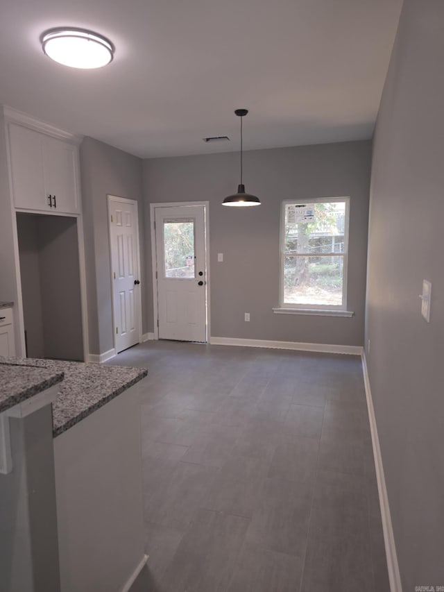 kitchen featuring light stone countertops, pendant lighting, and white cabinetry