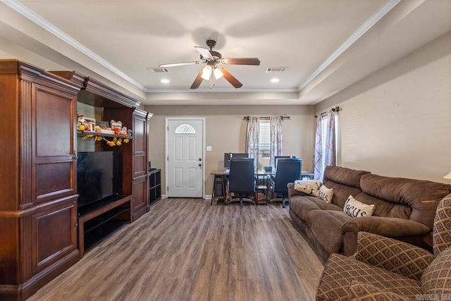 living room with ceiling fan, ornamental molding, a raised ceiling, and dark wood-type flooring