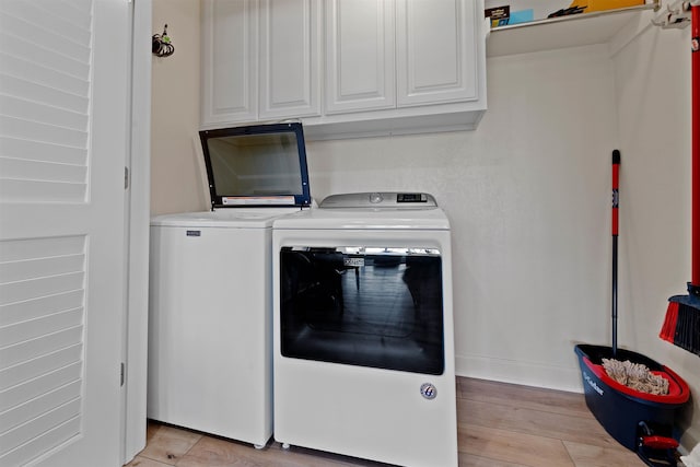 laundry area featuring light wood-type flooring, washer and dryer, and cabinets