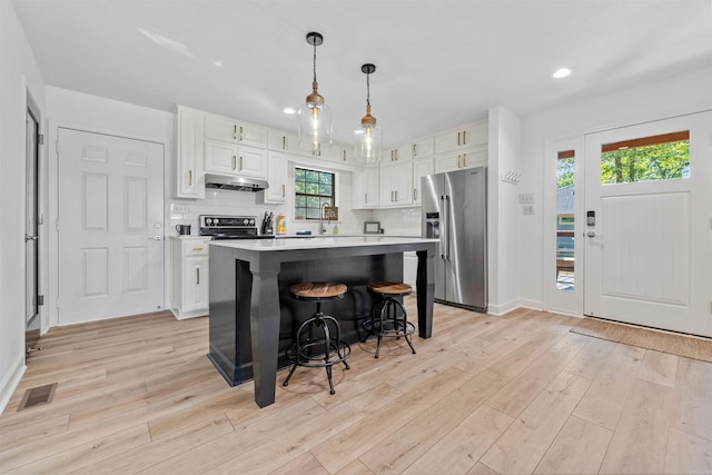 kitchen with white cabinets, a center island, hanging light fixtures, and stainless steel fridge