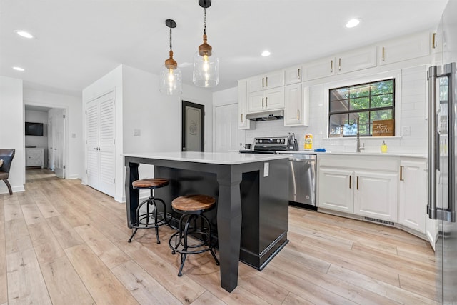 kitchen with white cabinets, appliances with stainless steel finishes, light hardwood / wood-style flooring, and a center island