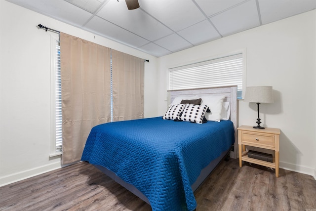 bedroom featuring a drop ceiling, dark wood-type flooring, and ceiling fan