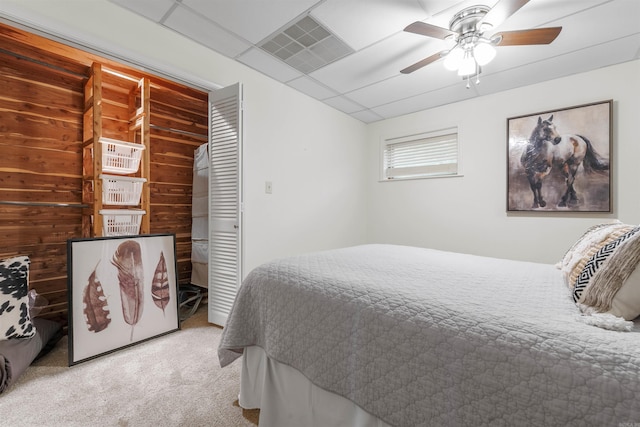 carpeted bedroom with a closet, wood walls, and ceiling fan