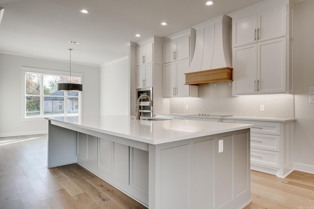 kitchen featuring custom range hood, a large island with sink, crown molding, and light hardwood / wood-style flooring