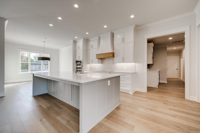 kitchen with a spacious island, white cabinets, decorative light fixtures, premium range hood, and light hardwood / wood-style floors