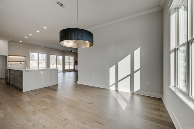 interior space featuring pendant lighting, crown molding, light wood-type flooring, and a center island with sink