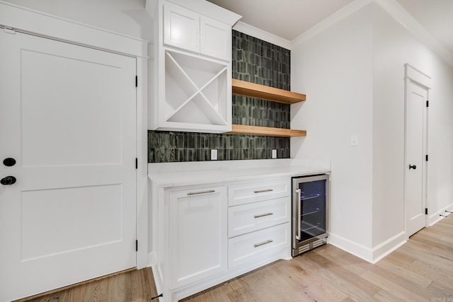 bar with light wood-type flooring, ornamental molding, white cabinetry, beverage cooler, and decorative backsplash