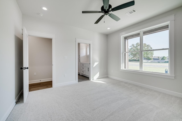 unfurnished bedroom featuring ceiling fan, light colored carpet, and ensuite bath