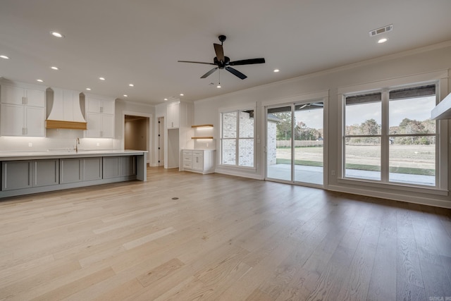 unfurnished living room with sink, crown molding, light hardwood / wood-style flooring, and ceiling fan