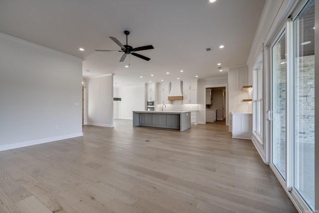 unfurnished living room featuring a wealth of natural light, ornamental molding, sink, and light hardwood / wood-style flooring