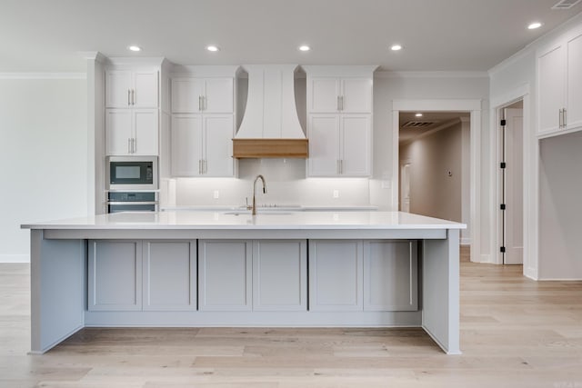 kitchen featuring a large island with sink, sink, custom range hood, and stainless steel appliances