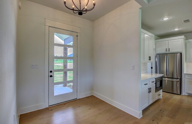 kitchen with light hardwood / wood-style floors, white cabinetry, an inviting chandelier, stainless steel appliances, and backsplash