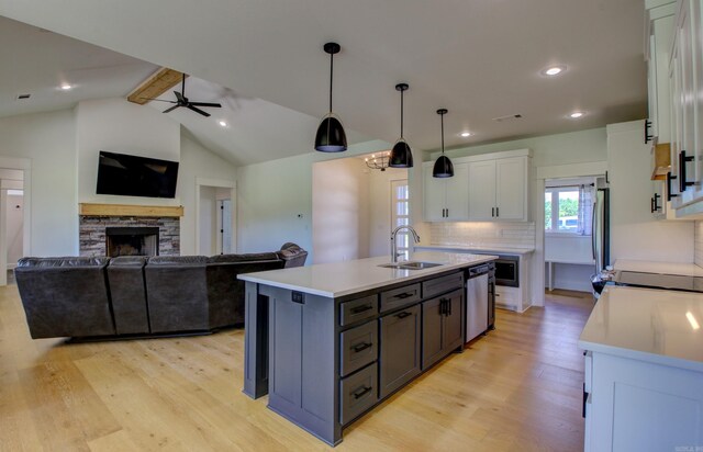 kitchen with vaulted ceiling with beams, decorative light fixtures, an island with sink, and white cabinets