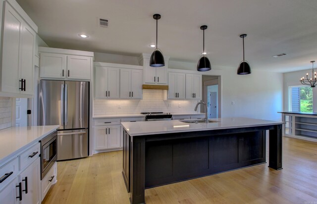 kitchen with light wood-type flooring, white cabinetry, a center island with sink, appliances with stainless steel finishes, and decorative light fixtures