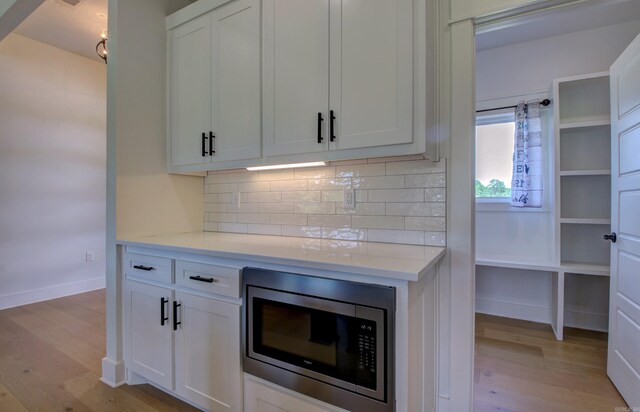 kitchen with white cabinets, light hardwood / wood-style flooring, stainless steel microwave, and decorative backsplash