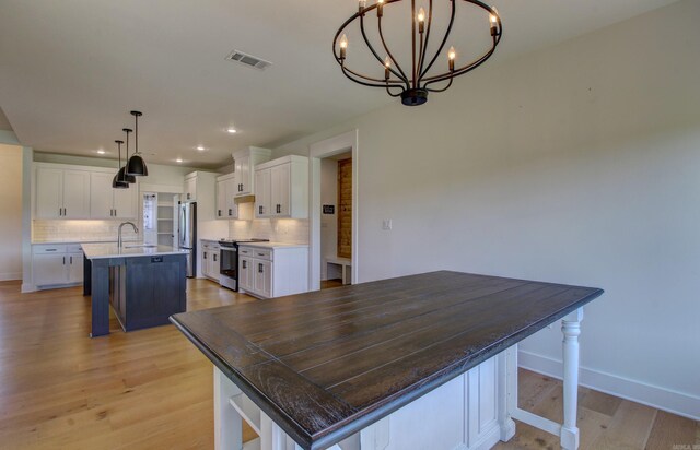 kitchen featuring white cabinets, a large island with sink, stainless steel appliances, a breakfast bar, and decorative backsplash