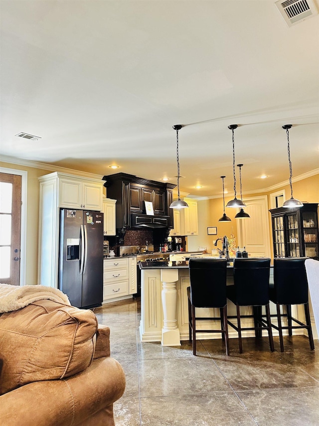 kitchen featuring pendant lighting, tasteful backsplash, stainless steel refrigerator with ice dispenser, a kitchen bar, and ornamental molding