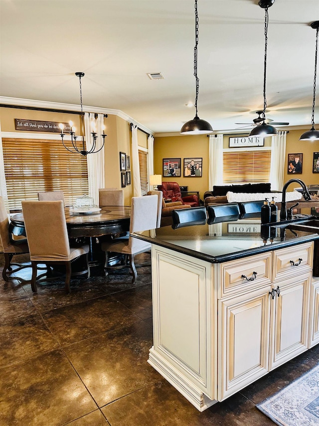 kitchen with ceiling fan with notable chandelier, a kitchen island with sink, sink, and pendant lighting