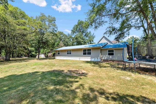 back of property featuring a trampoline and a lawn