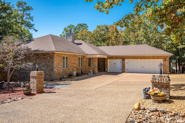 single story home featuring a garage, a chimney, concrete driveway, brick siding, and roof with shingles