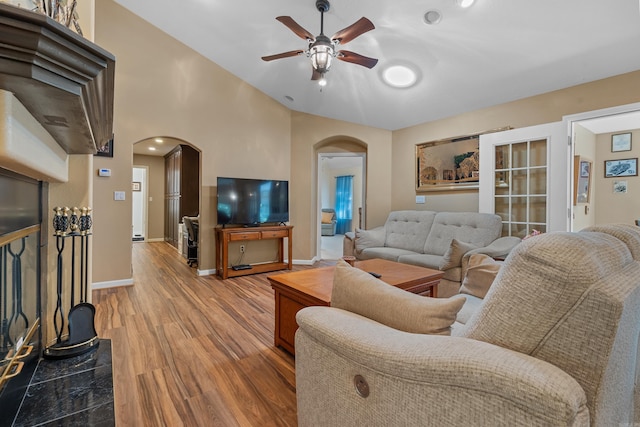 living area with baseboards, light wood-style floors, lofted ceiling, arched walkways, and ceiling fan