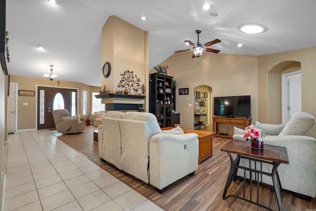 living area with a fireplace, arched walkways, a ceiling fan, lofted ceiling, and light wood finished floors