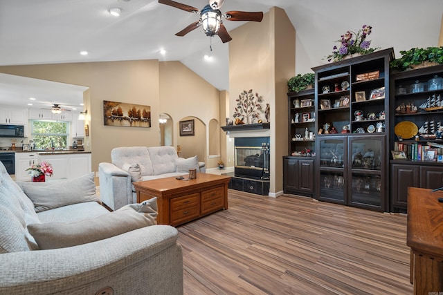 living room featuring arched walkways, a ceiling fan, wood finished floors, a tile fireplace, and lofted ceiling