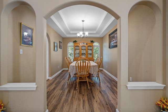 dining area featuring an inviting chandelier, dark wood finished floors, arched walkways, a raised ceiling, and baseboards