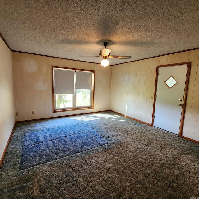 carpeted spare room with a textured ceiling, crown molding, wood walls, and ceiling fan