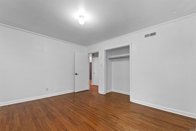 unfurnished bedroom featuring a closet, dark hardwood / wood-style floors, and crown molding