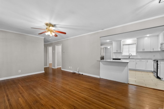 unfurnished living room featuring ornamental molding, light wood-type flooring, ceiling fan, and sink