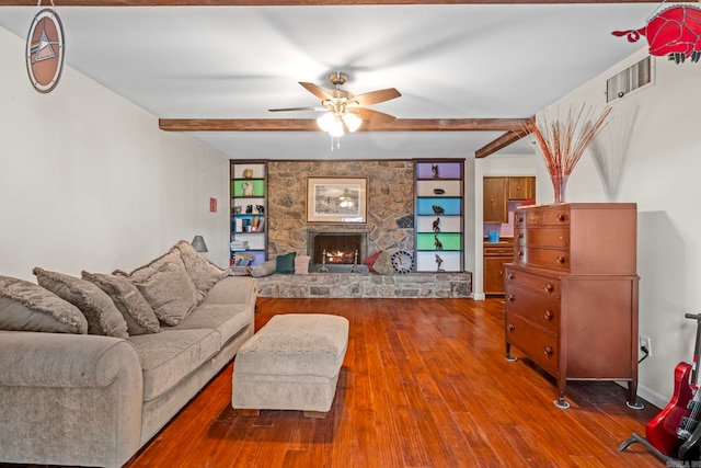 living room with ceiling fan, a stone fireplace, beam ceiling, and hardwood / wood-style floors