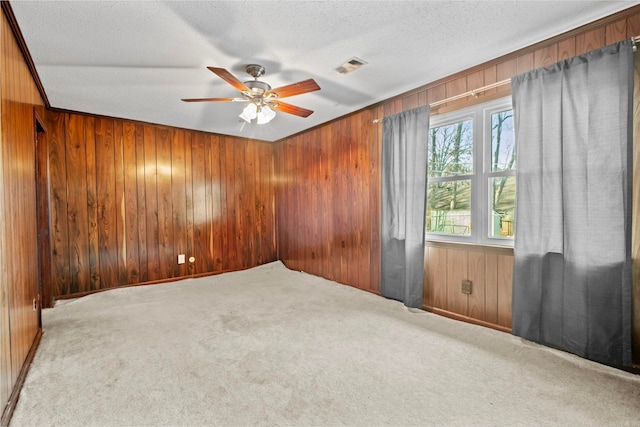 empty room with ceiling fan, a textured ceiling, wood walls, and carpet flooring