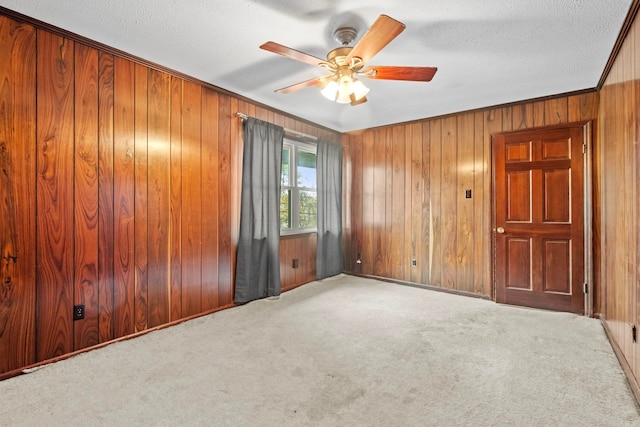 carpeted empty room featuring ceiling fan, a textured ceiling, and wooden walls