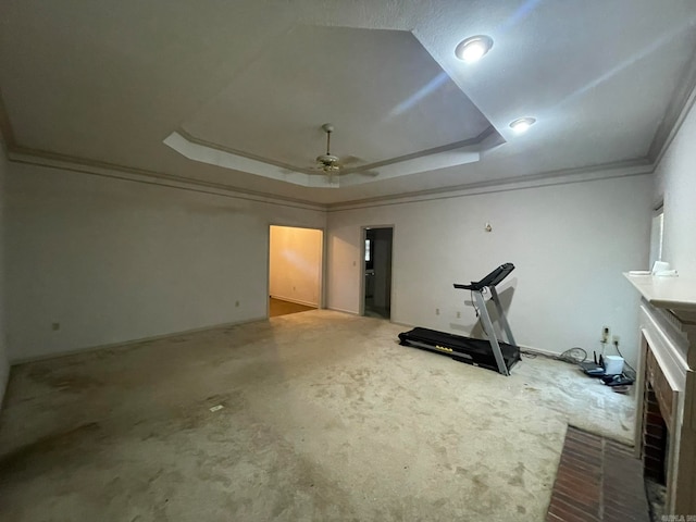 exercise room featuring a raised ceiling, a fireplace, ornamental molding, and ceiling fan