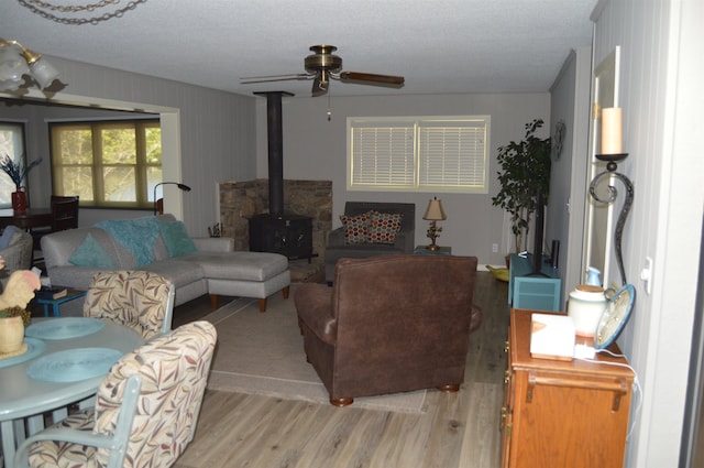 living room featuring ceiling fan, a textured ceiling, light hardwood / wood-style floors, and a wood stove