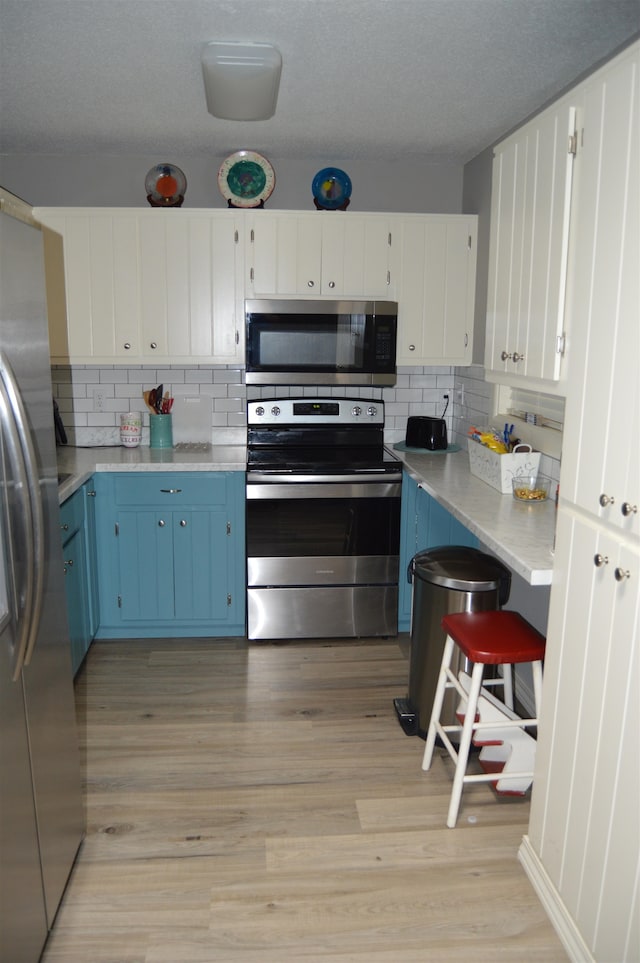 kitchen featuring light wood-type flooring, white cabinetry, blue cabinetry, and stainless steel appliances