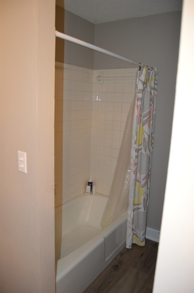 bathroom with a textured ceiling, hardwood / wood-style floors, and shower / tub combo with curtain