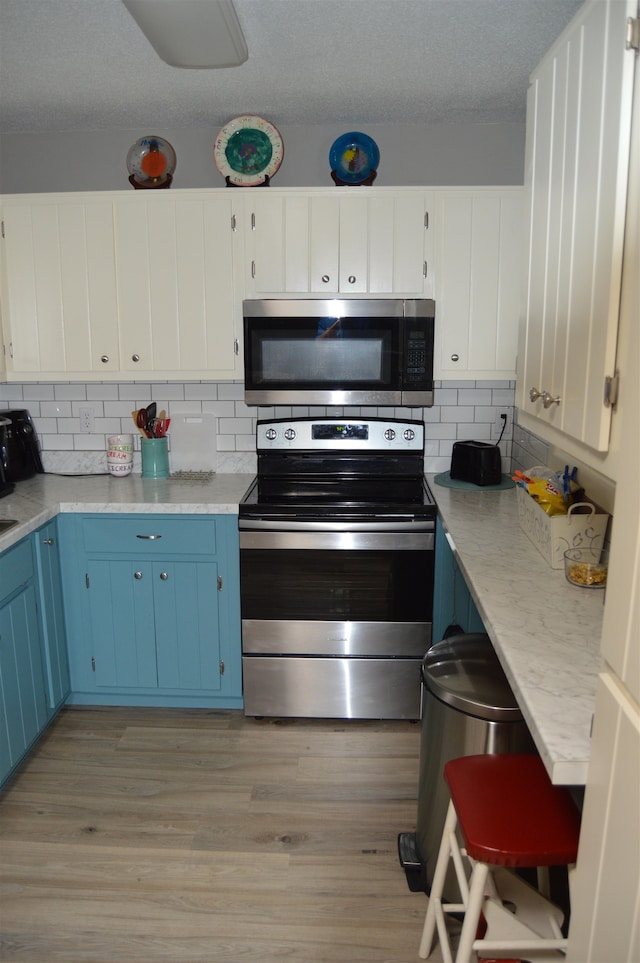 kitchen with light wood-type flooring, blue cabinetry, stainless steel appliances, and white cabinets