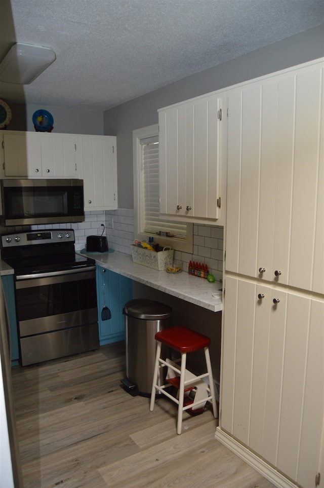 kitchen featuring appliances with stainless steel finishes, light wood-type flooring, white cabinetry, and decorative backsplash